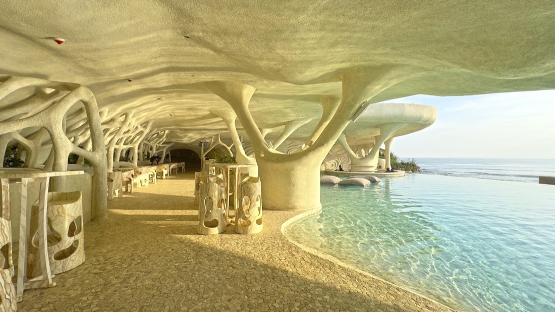 Cave-like pool terrace at Luna Beach Club with pale organic tree-form columns and an infinity pool meeting the ocean horizon