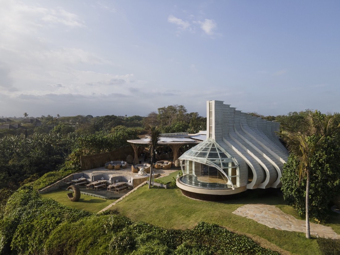 Glass-and-shingle ceremonial pavilion at Luna Beach Club set in green lawns with a shaded lounge
