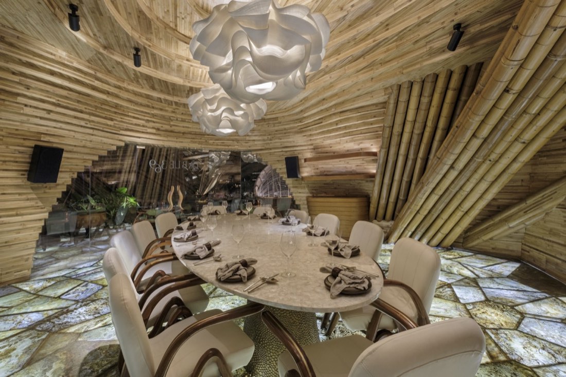 Bamboo-clad private dining room at Luna Beach Club with a round stone table under a swirling timber ceiling and a sculptural pendant light
